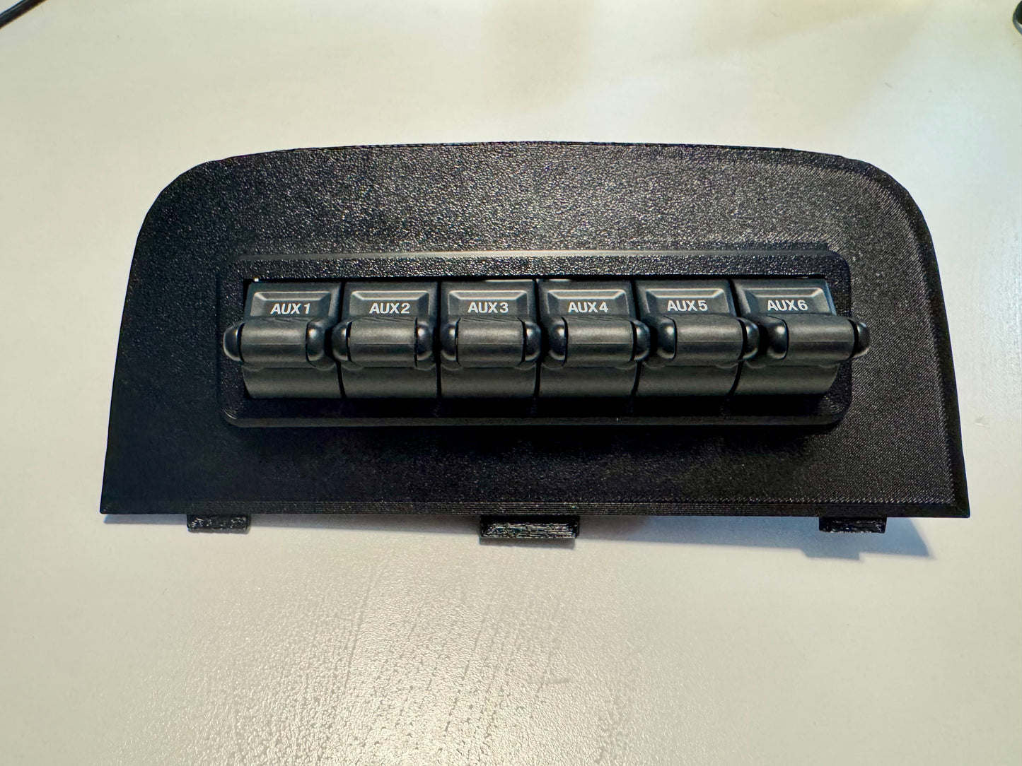 A black textured plastic dashboard trim piece with a rectangular cutout, photographed on a light off-white surface.